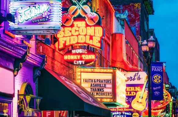 	lit neon signs for bars and clubs hanging from the business fronts in Nashville